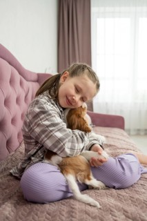 A young girl lovingly embraces her small dog on a plush sofa, sharing a warm and joyful moment at