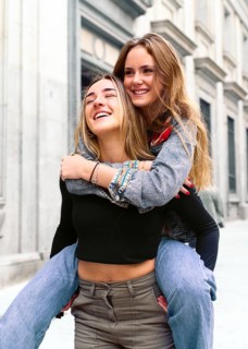 Two young women share a joyful moment in a lively city street. Their happiness and connection are
