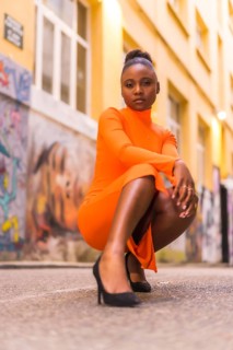 Fashionable urban style with a black African girl in an orange dress and black heels on a city