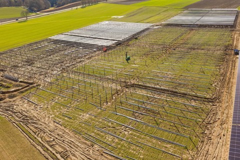 Solar system under construction on a large field with visible metal structures and grass, Agri PV