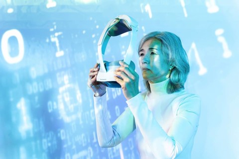 An elderly Asian woman immerses herself in the metaverse using a VR headset. The digital background