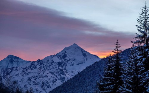 A breathtaking view of a snow-capped mountain at sunrise, glowing in warm hues of orange and pink