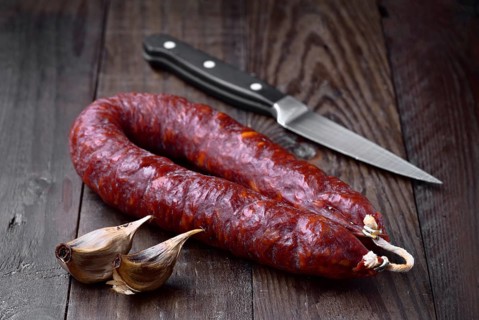 A spanish chorizo sausage rests on a rustic wooden table, accompanied by two cloves of garlic and a