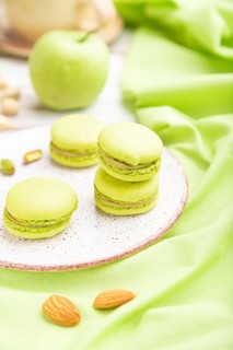 Green macarons or macaroons cakes with cup of coffee on a white wooden background and green linen