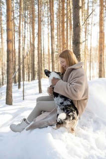 A woman plays lovingly with her Border Collie dog amidst the snowy forest. Captured in daylight,