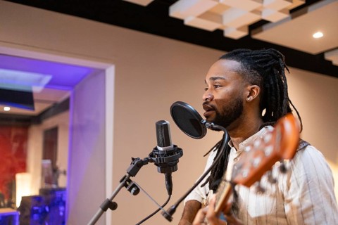 A black musician passionately sings into a microphone while playing guitar in a professional