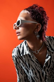 Fashion model wearing animal print shirt, white sunglasses, and silver accessories in front of a