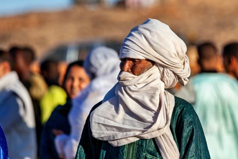 Man with turban looks to the side, surrounded by people, The traditional Tuareg at the Tamanrasset