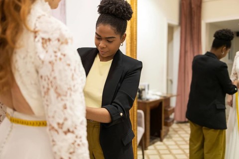 A seamstress skillfully adjusts a lace dress on a client in a tailor studio. The setting is