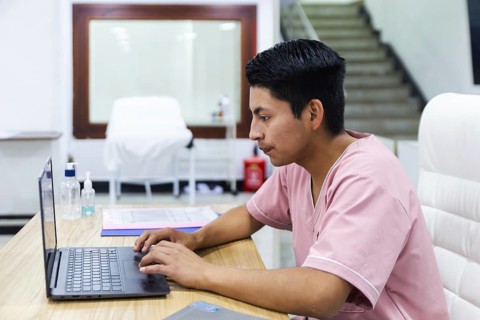 A professional in a physiotherapy clinic in Ecuador works diligently on a laptop. The modern, clean