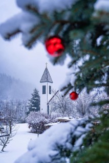 Focus on red balls and snowy branches in front of a church tower in the background, Enzklösterle,
