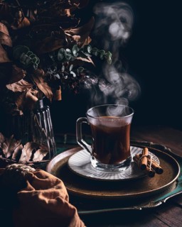 Steaming coffee in a glass mug with aromatic cinnamon sticks on a saucer, accompanied by a rustic
