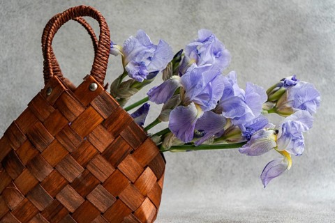 Close-up view of a brown woven basket accompanied by blooming Iris flowers, presented on a textured