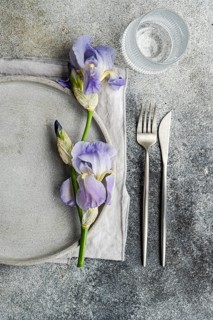 From above, an elegant table setting features a purple iris flower alongside a gray ceramic plate,