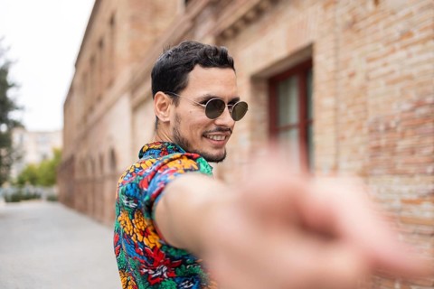 A cheerful Cuban man wearing a colorful shirt and sunglasses, smiling outdoors. The vibrant