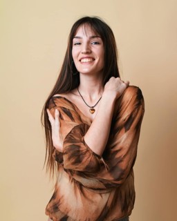 Portrait of a young woman on a beige background, captured in a studio setting. She is smiling and