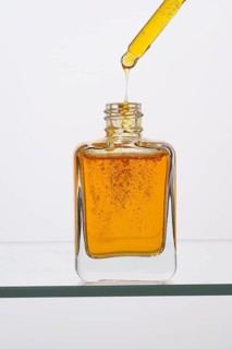 Close-up of a glass bottle containing vitamin C serum with a pipette dispensing drops The golden