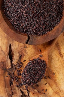 Natural black rice in a wooden bowl and spoon on a wooden surface in rustic style, top view