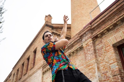 A Cuban man, dressed in a colorful shirt, passionately dances against a historic brick building