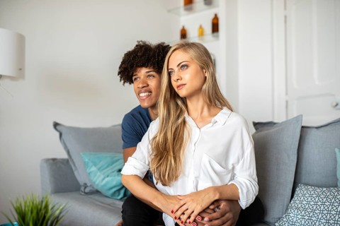 A couple sits closely on a comfortable sofa, sharing a peaceful moment. They appear relaxed and