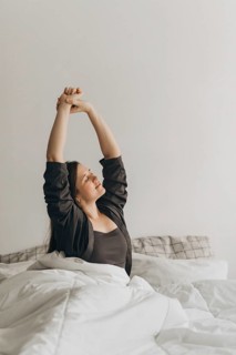 Woman stretching in bed, embracing a fresh start to her day. The image symbolizes a healthy morning