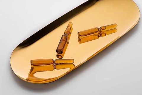 Three amber-colored cosmetic ampoules containing anti-aging serum, elegantly displayed on a