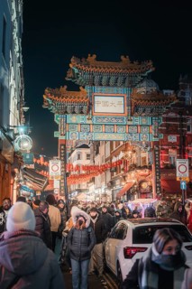 Chinese gate at night, illuminated decorations and lots of passers-by, New Year's Eve London,