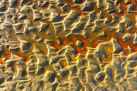 Aerial image of sand dunes showcasing intricate textures and patterns, highlighted by warm, golden
