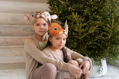 Two children, a boy and a girl, wearing animal masks, sit together in front of a decorated