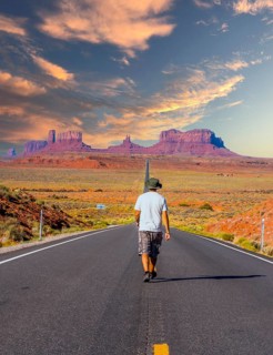 A young man in a white shirt walking on the road to Monument Valley in sunset. Utah