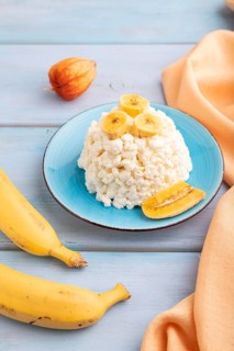 White ?ottage cheese, Curd, with Banana on blue wooden background and orange textile, side view,