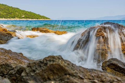 Wellen brechen an einem Felsen im Meer an einem sonnigen Tag auf der Insel Cres, Kroatien