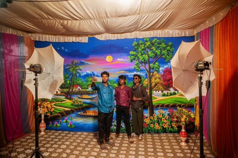 Three teenagers are taking pictures of themselves in an itinerant photo studio. Photographed in