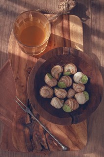 Snails cooked with herb oil on a wooden plate, served with white wine, natural light, no people
