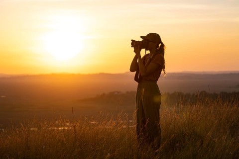Young woman taking pictures at sunset, standing in tall grass, landscape, view of Lake Victoria and