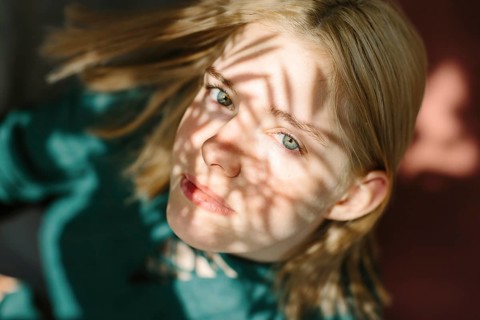A captivating portrait of a teenager with sunlit shadows creating patterns on their face, producing