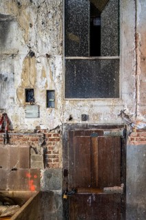 A close-up of an old wooden door set within a deteriorating wall with peeling plaster, exposed