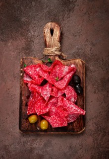 Sliced salami sausage, on a wooden chopping board, decorated with olives and herbs, close-up, no