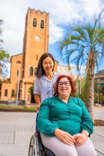 Asian woman pushing the wheelchair of a friend along downtown in the city