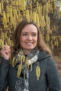 Happy young Caucasian woman without allergy problem standing by flowering hazel bush in Ystad,