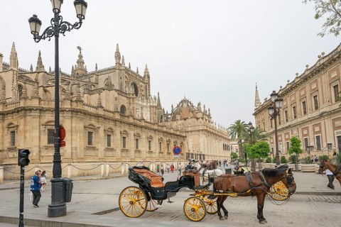 Historic street scene with horse-drawn carriages and Gothic architecture in the background,