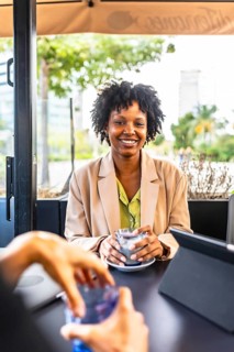 Vertical portrait of a happy successful african businesswoman drinking latte sitting in a cafeteria