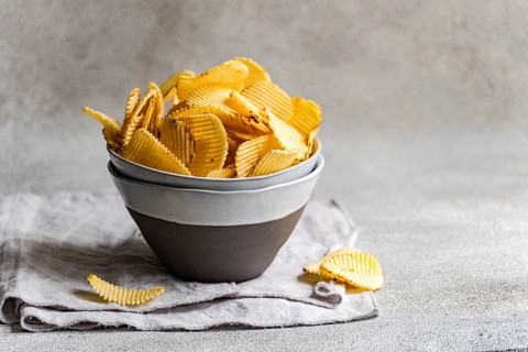 A bowl of delicious homemade potato chips, perfectly golden and crispy, sits on a neutral gray