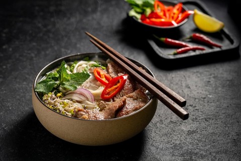 Traditional Vietnamese Beef Pho Noodle Soup in a ceramic bowl, garnished with slices of beef,