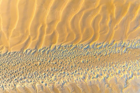 Aerial shot of sand dunes showcasing wavy patterns and textures in a desert landscape. The sun