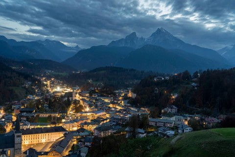 Berchtesgaden glows with warm lights against the dark silhouette of the Watzmann mountain This