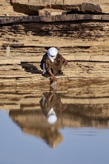 A person draws water from a rock in a desert-like environment, Tuareg collecting water in the