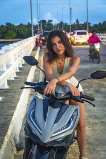 Tourist enjoying her scooter on afam bridge, siargao island, philippines, during a tropical sunset