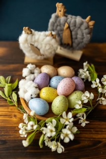 A rustic setting featuring colorful speckled Easter eggs in a wooden bowl, surrounded by white