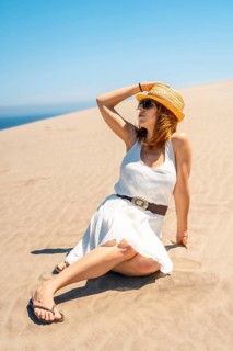 Vertical photo of a Woman holding sun hat sitting outdoors on a windy day in Cabo de Gata, Spain